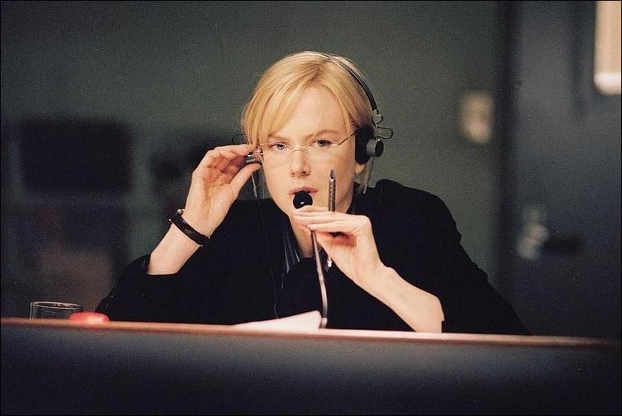 Nicole Kidman in a scene from 'The Interpreter'. She is wearing glasses, headphones and speaking into a microphone while holding a pen.