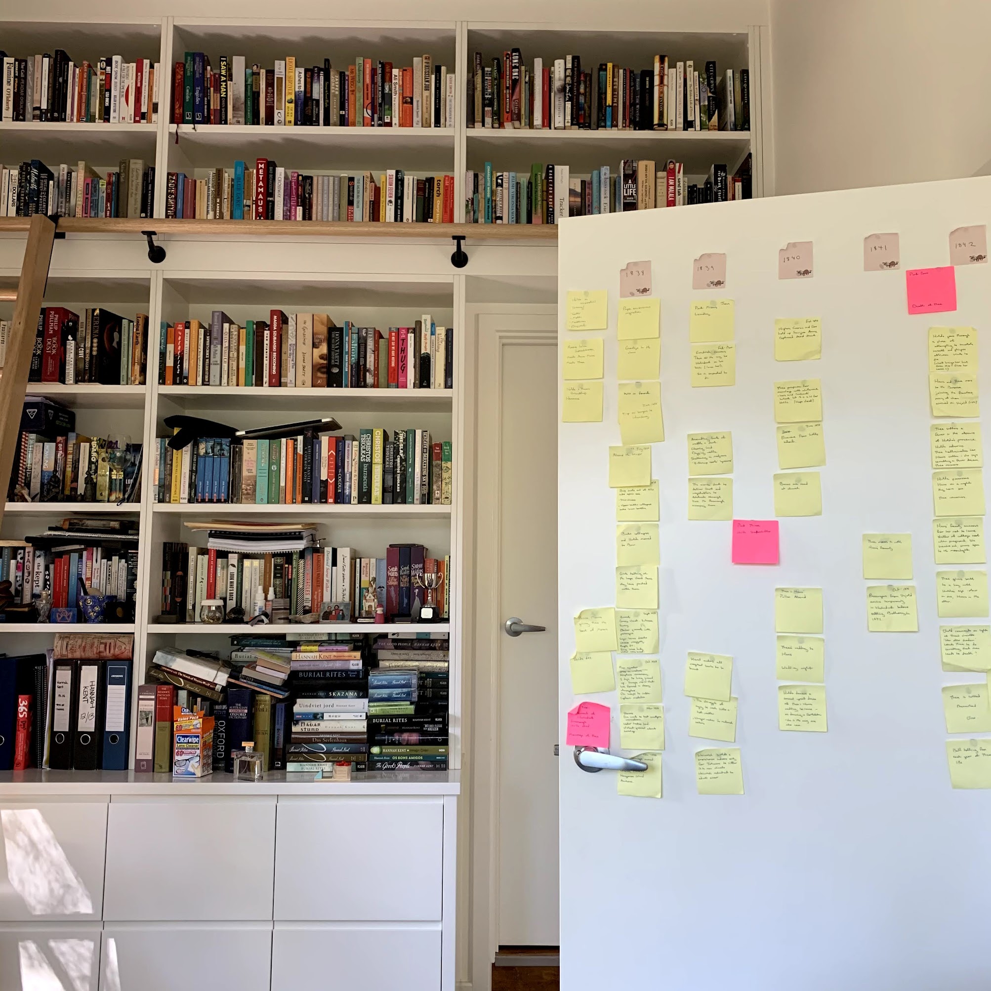 A wall of white floor to ceiling bookshelves filled with books. In front of them is a door covered in yellow and pink post-it notes.