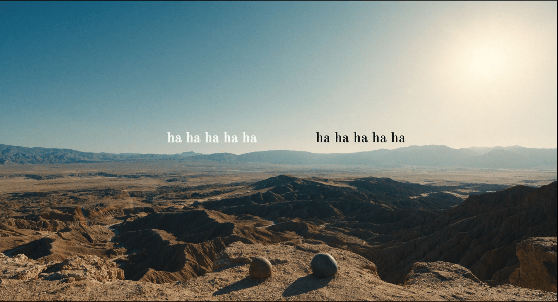 A still from Everything Everywhere All At Once. two small rocks (representing two characters) sit on a cliff top. Above each rock is the text "ha ha ha ha ha".