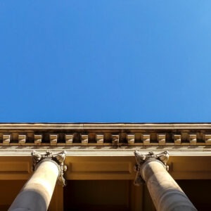 A photo taken looking upwards of the columns of the old Adelaide Supreme Court building against a blue sky.