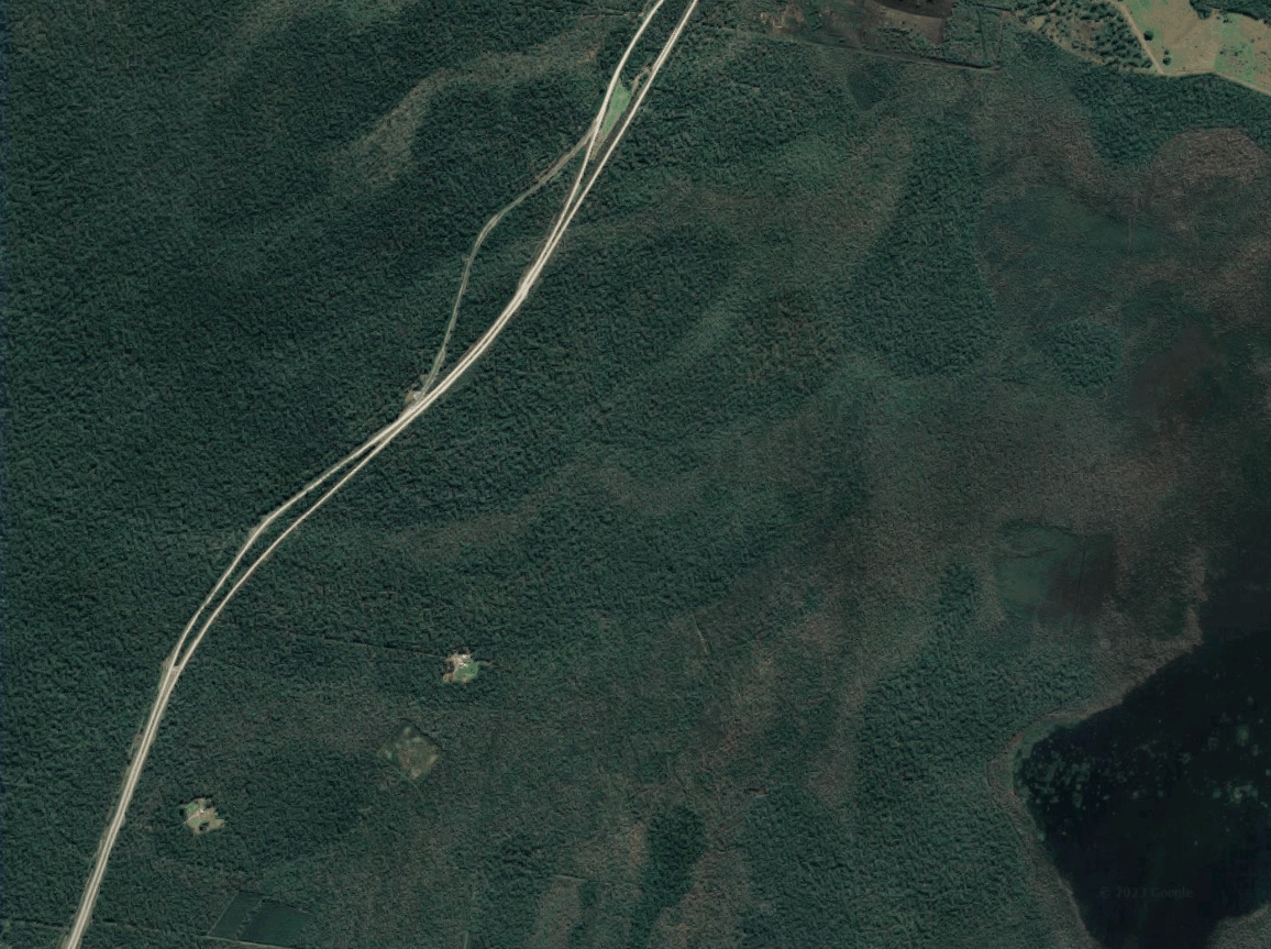 A satellite photograph of a white road intersecting dark green bushland.