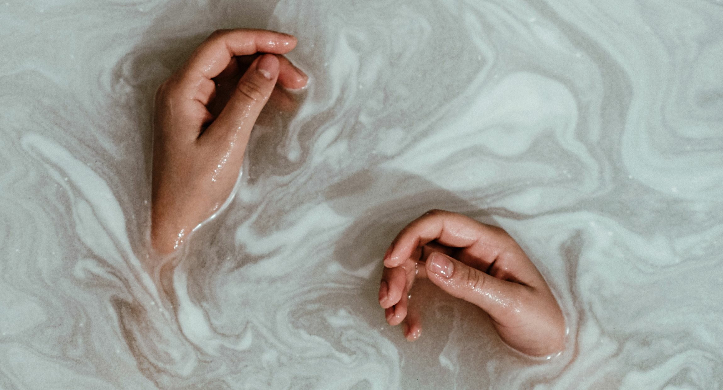 Two hands rest in soapy bathwater.