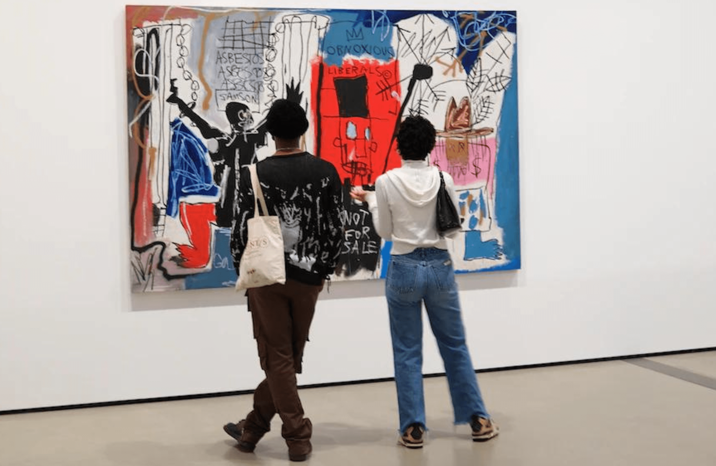 Two young Black people have their backs turned to the camera and are looking at a Basquiat painting. It is abstract and in the centre, at the bottom, it reads 'Not for Sale'.